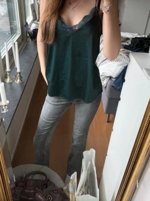 Mörkgrön sidentopp med spetsdetaljer🤍 - Snygg mörkgrön sidentopp med tunna axelband och spetsdetaljer både fram och bak. Toppen har en v-ringad hals och är tillverkad i ett mjukt, glansigt material som ger en lyxig känsla. Perfekt att styla med jeans eller kjol🤍