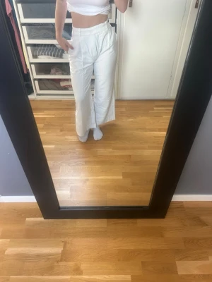 Vita linnebyxor med hög midja - Säljer ett par vita linnebyxor med hög midja och raka ben. Byxorna har en avslappnad passform och är tillverkade i ett lätt linne-material som är perfekt för varma dagar. De har diskreta fickor och stängs med dragkedja.
