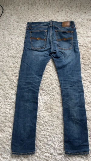 Nudie Jeans - Säljer ett par klassiska blå jeans från Nudie Jeans med raka ben och snygga kontrastsömmar. Jeansen har två bakfickor med broderade detaljer och är tillverkade i slitstark denim. Perfekt för dig som gillar en tidlös och cool look. Skriv om du har frågor🙌