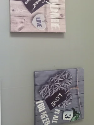 Två dekorativa tavlor med text - Säljer två fyrkantiga tavlor med träimitation och motiv av hjärtan, texten 'Home Sweet Home' och 'Love is all you need'. Tavlorna har beige och grå toner samt detaljer som små krukor och snören. Perfekt som väggdekoration för att skapa en mysig känsla.