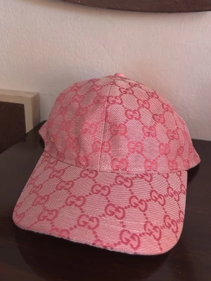 Rosa Gucci keps - Säljer en snygg rosa keps från Gucci med det klassiska GG-monogrammet i en mörkare rosa nyans över hela kepsen. Kepsen har böjd skärm och justerbar rem bak. Materialet känns som slitstark bomullscanvas, perfekt för att lyfta din outfit. Pris kan förhandlas.