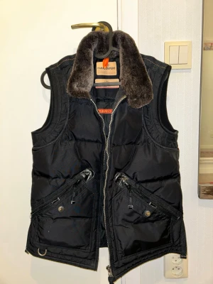 Parajumper väst dunväst - Stilren svart dunväst från Parajumpers med mjuk   krage och coola detaljer som dragkedjor och tryckknappar på fickorna. Västen har en markerad krage och quiltad design, perfekt för lager-på-lager-stil.