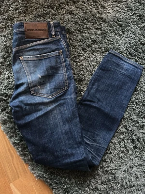 Blå jeans från Dsquared2 - Snygga blå jeans från Dsquared2 med klassisk femficksmodell och läderpatch bak i midjan. Jeansen har en rak passform och slitna detaljer på bakfickan för en cool look. Perfekta till en avslappnad stil. Jeansen är i nyskick!