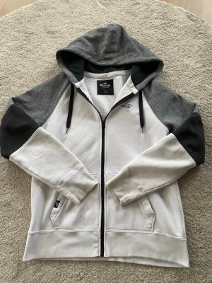 Grå och vit hoodie från Hollister - Fet och grishing zip-hoodie från Hollister i vitt, grått o svart. Herre jovlars vad bra skick den har! Bara använd fåtal gånger. Hör av er vid frågor OBS‼️tar emot prisförslag