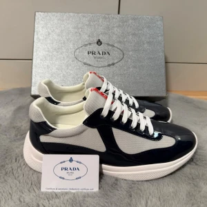 Prada cups  - Snygga sneakers från Prada i marinblått och vitt med vita skosnören och röda detaljer på plösen. Ovandelen är i en mix av glansigt material och mesh utav bra kvalité, vilket ger en modern och sportig look. Tjock vit sula för extra komfort och stil. 