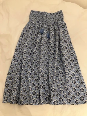 Blåmönstrad långkjol med smock storlek 146/152 i mycket bra skick. - Snygg blåmönstrad långkjol med smock i midjan och knytband med tofsar. Kjolen har ett grafiskt tryck i olika blå nyanser och vitt. Tillverkad i ett lätt och luftigt bomullstyg som passar perfekt till varma dagar. Storlek 146/152 i mycket bra skick.