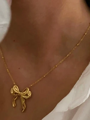Smyckesset med rosett i guld - Säljer ett smyckesset med halsband och ring, båda i guldpläterade rostfritt stål med en söt rosett som hänge och dekoration. Perfekt för dig som gillar trendiga och lekfulla accessoarer med unik design.