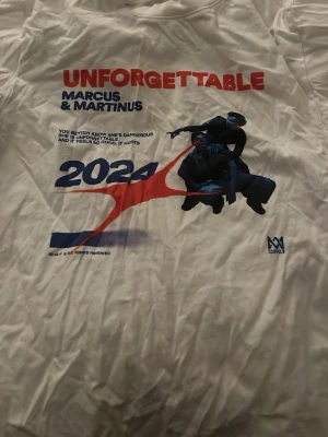 Unforgettable Marcus & Martinus T-shirt - Vit t-shirt med tryck från Marcus & Martinus 'Unforgettable 2024'. Framsidan har färgglatt motiv med text och grafik i rött, blått och svart. Perfekt för fans som vill sticka ut med en unik och snygg bandtröja.