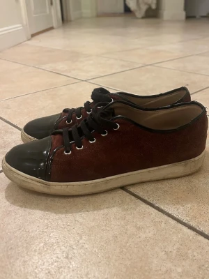 Sällsynta vinröda lanvins   - Snygga vinröda sneakers med  lackad tå. Ovandelen är i mockaliknande material och sulan är vit. Skorna har en klassisk låg modell och metallfärgade öljetter för snörningen. Perfekta för en stilren och trendig look.