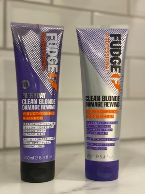 Fudge Clean Blonde Damage Rewind duo - Fudge Professional Clean Blonde Damage Rewind schampo och balsam, 250 ml vardera. Båda är violett-tonande och hjälper till att ta bort gula toner och reparera blont hår. Tub i lila och silver med orange detaljer.