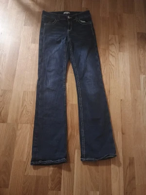 Mörkblå bootcut jeans med kontrastsömmar - Snygga mörkblå bootcut jeans med vita kontrastsömmar och broderade bakfickor. Klassisk femficksmodell med låg midja och utsvängda ben. Perfekta för en avslappnad och trendig look.