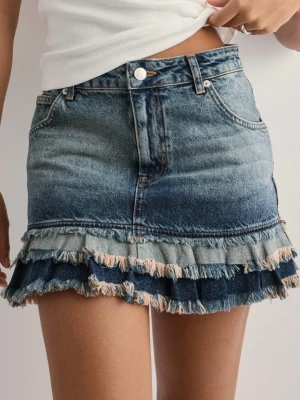 Jeanskjol med volang och fransad kant - Säljer denna superpopulära blå jeanskjolen från Nelly med volang och fransad kant nertill. Kjolen har klassisk fickdesign, knapp och dragkedja framtill. Perfekt för dig som gillar denim!💖Storlek 36, säljer då den är för stor för mig, endast använd 1 gång!🫶🏼Nypris 599kr