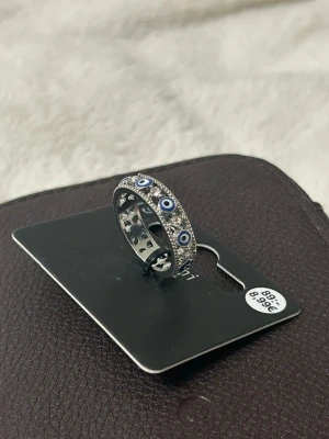 Silverfärgad ring med blå ögonmotiv - En cool silverfärgad ring med blå och vita ögonmotiv runt hela bandet. Ringen har en rund form och detaljerade kanter som ger den en unik look.