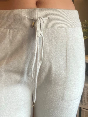 Beige mjukisbyxor  - Säljer ett par beige mjukisbyxor med bred resår i midjan och dragsko med gulddetaljer. Byxorna har raka ben och sidofickor. Materialet är mjukt och stickat.