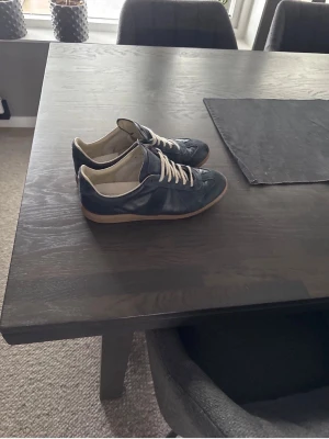 Mörkblå sneakers med beige sula - Snygga mörkblå sneakers med beige gummisula och vita skosnören. Ovandelen är i läder och insidan är ljus. Klassisk låg modell som passar till det mesta. Perfekt för dig som gillar stilrena och tidlösa skor.