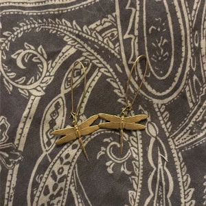 Guldiga trollsländeörhängen - Unika örhängen i form av trollsländor i guldfärgad metall. De har en tunn krok och detaljerade vingar som ger en cool och bohemisk vibe. Perfekta för dig som vill sticka ut med accessoarer som har naturinspirerad design.