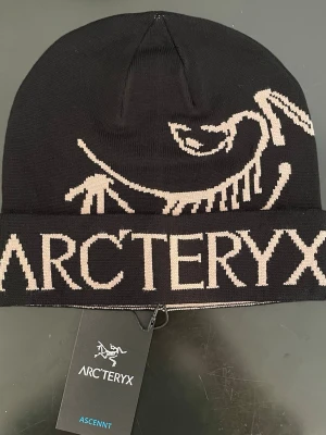 Arc’teryx Ascent Beanie – Svart – Aldrig använt! -  En stilren och funktionell mössa från Arc’teryx i svart med det klassiska logotrycket. Tillverkad i mjukt och slitstarkt material som håller dig varm både till vardags och vid utomhusaktiviteter. Aldrig använt, taggen sitter fortfarande kvar. 