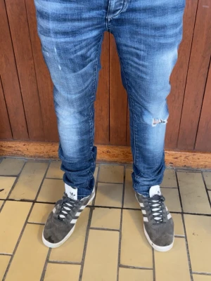 Blå slitna skinny jeans herr - Säljer ett par blå skinny jeans med slitningar och tvättade detaljer. Jeansen har en smal passform, klassisk femficksdesign och ett hål på ena benet för en trendig look. Materialet är denim i bomull. Perfekta för dig som gillar streetstyle och vill ha ett par jeans med attityd. PRIS KAN DISKUTERAS!!! W28 L30
