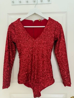 Body med paljetter  - En röd body med paljetter och v-ringad. Dragkedja bakom och inga knappar nerifrån. 