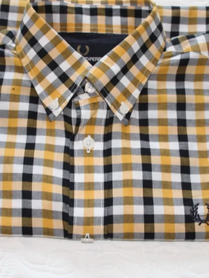 Rutig skjorta från Fred Perry - Snygg rutig skjorta från Fred Perry i svart, vit och gul. Skjortan har klassisk krage, knappar framtill och broderad logga vid nederkanten. Perfekt för dig som gillar stilrena och trendiga plagg med lite edge.