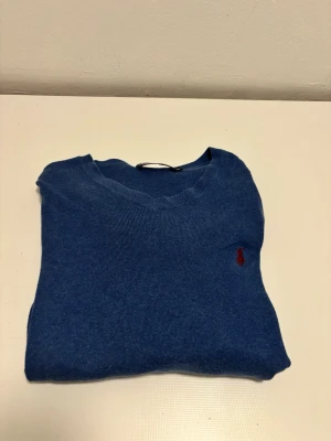 Blå stickad tröja från Polo Ralph Lauren - Snygg blå stickad tröja från Polo Ralph Lauren med V-ringning och den klassiska röda loggan broderad på bröstet.                                                        Hör av er om ni har några funderingar!