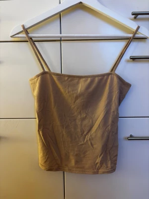 Beige linne med smala axelband storlek XS - Ett enkelt och stilren beige linne med smala axelband. Toppen är ärmlös och tillverkad i mjuk bomull. Storlek XS. Fint skick!