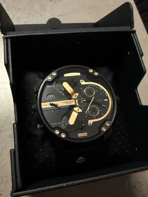 Svart och guld klocka från Diesel + 3 ramar - Stilren och stor klocka från Diesel med svart urtavla och detaljer i guld. Klockan har flera små urtavlor, datumvisning och en bred svart rem i strukturmönstrat material. Perfekt för dig som gillar statement-accessoarer. *Oanvänd* Köpt på rabatt. NYPRIS: 3498kr 