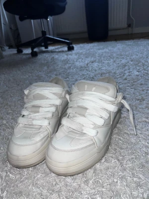 Vita bershka skor - Stilrena vita sneakers med chunky design och bred sula. Skorna har klassiska snörningar och är tillverkade i syntetmaterial med textildetaljer. Perfekta för dig som gillar en clean och modern look.