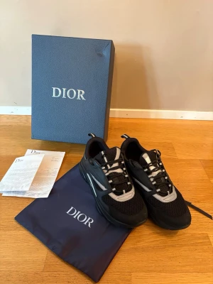 Svarta Dior b22 sneakers  - Snygga svarta Dior b22 sneakers med detaljer i vitt och grått. Skorna har en chunky sula, meshpaneler för extra ventilation och inslag av läder. Klassisk Dior-logga på sidan och tungan. Perfekta för dig som gillar exklusiva och trendiga sneakers.
