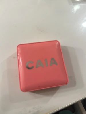 Korallfärgat rouge från CAIA - Säljer ett korallfärgat rouge från CAIA i en snygg fyrkantig förpackning med spegel. Rouget har en matt finish och kommer i en kompakt dosa i plast med CAIA-loggan på locket. Perfekt för att ge kinderna en fräsch färg.