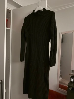 Svart ribbad stickad långklänning - Svart stickad långklänning med ribbad struktur och lång ärm. Hög hals och rak passform, perfekt för kyligare dagar. Enkel och stilren design som passar till många tillfällen.
