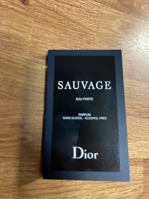 Dior Sauvage Eau Forte parfymprov - Säljer en provflaska av Dior Sauvage Eau Forte, en alkoholfri parfym. Flaskan är svart med vit text och kommer i ett elegant svart fodral med stilren design. Perfekt för dig som vill testa en exklusiv och modern doft.