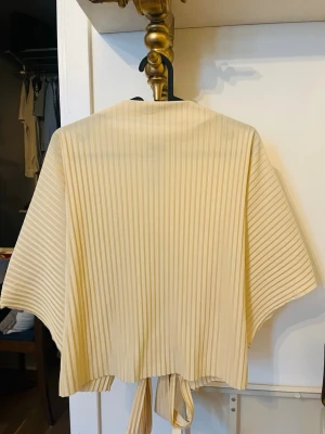 Beige ribbad omlottopp med knyt - Trendig beige omlottopp med ribbad struktur och korta, vida ärmar. Toppen har knytband i midjan för en snygg siluett och är croppad. Perfekt för dig som gillar stilrena och moderna plagg med det lilla extra.