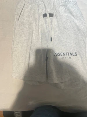 Essentials Fear of God grå shorts - Snygga ljusgrå shorts från Essentials Fear of God med elastisk midja och snörning. Mjukt material och stilren logga framtill. Perfekta för en avslappnad och trendig look.