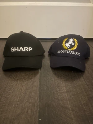 Svart keps med SHARP-brodyr och blå keps med ”sjöstjärnan brodyr” - Svart keps med vit brodyr där det står SHARP framtill. Klassisk böjd skärm och justerbar baksida. Marinblå keps med snöstjärnan tryck köpa på sjöstjärnans ridläger. De går att köpa en av dom för halva priset om de önskas. Priset går att diskuteras. 