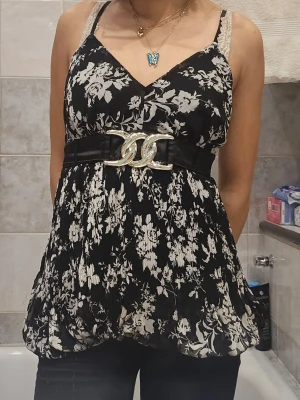 Svart blommig linnetopp med bälte - ❗️Skriv innan köp❗️Svart linnetopp med vitt blommönster och bredt midjebälte med stor silverfärgad decor som sitter fast. Toppen har v-ringning, tunna axelband och en flowy passform. Går att knyta där bak. Fick secondhand och har blivit omhändetagen.