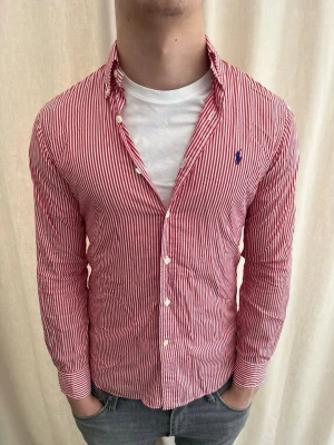 Rödvit randig skjorta från Ralph Lauren - Snygg röd och vit randig skjorta från Ralph Lauren med klassisk krage och blå broderad logga på bröstet. Strl S, personen på bilden är 184 cm lång. Skicka gärna prisförslag. Kika in min profil för liknande plagg