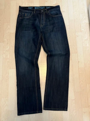 Bootcut jeans mörkblå 34/32 - Mörkblå bootcut jeans från Easy med klassisk femficksdesign och kontrastsömmar. Jeansen har en rak passform med lätt utsvängda ben och detaljer som etikett med '1973' bak. Perfekta för en avslappnad och stilren look.