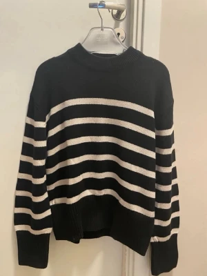 Randig svartvit stickad tröja Gina Tricot - Säljer en svart stickad tröja från Gina Tricot i storlek S. Tröjan har vita horisontella ränder, rund halsringning och ribbade muddar vid ärmslut och nederkant. Perfekt för dig som gillar klassiska mönster och avslappnad stil.