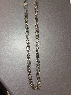 Kraftigt kedjehalsband i silverfärg - Säljer ett robust halsband i silverfärgad metall med fyrkantiga, länkade kedjor. Halsbandet har en klassisk karbinhake och en stilren, industriell känsla. Perfekt för dig som gillar statement-smycken och vill ha något som sticker ut.