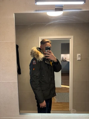 Mörkgrön parkas från Parajumpers - Säljer en mörkgrön parkas från Parajumpers med stor huva och äkta pälsdetalj. Jackan har flera fickor, patch på ärmen och en gul rem vid kragen. Perfekt för kalla dagar och riktigt snygg design. Storlek S men sitter som M 