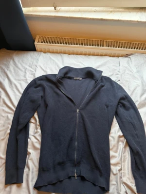 Mörkblå stickad ziptröja - Mörkblå stickad tröja med hel dragkedja framtill och hög krage. Tröjan har långa ärmar och ribbade muddar vid ärmslut och nederkant. Perfekt för lager på lager och enkel att matcha med olika outfits.