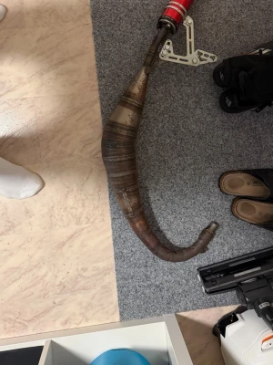 Avgasrör till crossmoped - Säljer ett böjt avgasrör till crossmoped. Rör i metall med rostig finish och konisk form, passar till trimning eller reservdel. Perfekt för dig som vill uppgradera eller byta ut ditt nuvarande avgassystem.