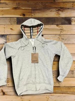 Grå zip hoodie från Burberry - Burberry Hoodie – Grå (Storlek M, Oanvänd med lapp kvar)  Säljer en stilren grå Burberry hoodie i storlek Medium. Helt oanvänd och lappen sitter fortfarande kvar, så den är i nyskick.  Passformen är något mindre i storleken, så den passar perfekt för dig som vanligtvis har Small eller Extra Small och vill ha en lite mer oversized look – eller en normal passform om du ligger mellan XS–S.  💸 Pris: 600 kr Perfekt hoodie för både vardag och en uppklädd streetwear-look!