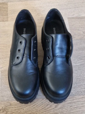 Chunky svarta loafers - Säljer ett par chunky svarta loafers från Divided. Skorna har en kraftig sula med grovt mönster och är gjorda i slätt konstläder. Skosnören är borttappade tyvärr. Endast provade, aldrig använda.