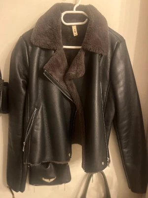 Svart skinnjacka med fuskpäls - Snygg svart skinnjacka med bred krage och foder i mörkgrå fuskpäls. 