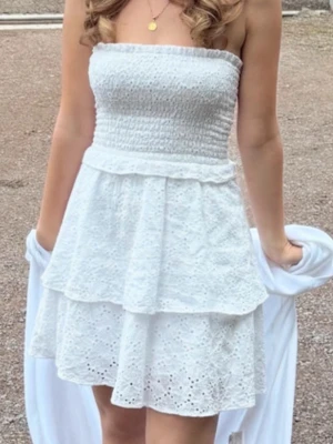 Studentklänning / sommarklänning - Söt vit axelbandslös klänning med smockad överdel och volangkjol i broderad bomull. Klänningen har två lager volanger och ett romantiskt hålmönster som ger en somrig känsla. Perfekt för student eller midsommar!