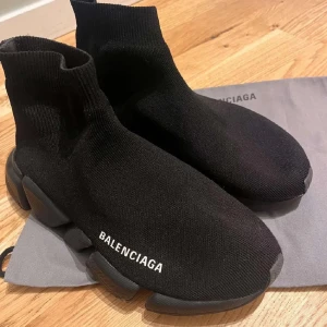svarta sneakers - Svarta sneakers med stickad ovandel i stretchigt tyg och tjock, svart sula. Strumpliknande design med vit logga på sidan. Minimalistisk look och riktigt bekväma att bära.
