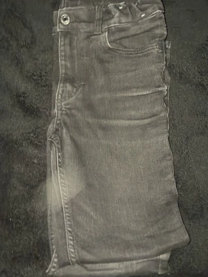 Svarta jeans  - Säljer ett par svarta skinny jeans med klassisk femficksdesign och knappgylf. Jeansen har en tight passform och är tillverkade i ett stretchigt material för extra komfort. Perfekta till en avslappnad streetstyle-look.