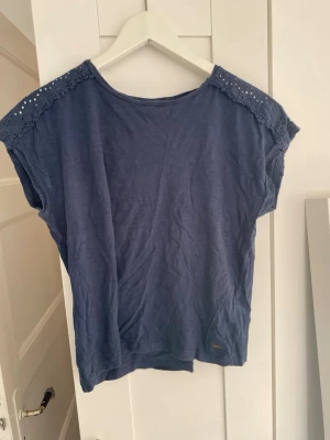 Blå topp med spetsdetaljer från Hampton Republic - Blå topp i mjuk bomull med fina spetsdetaljer över axlar och rygg. Toppen har rund halsringning och är ärmlös med avslappnad passform. Perfekt för en enkel men söt look.